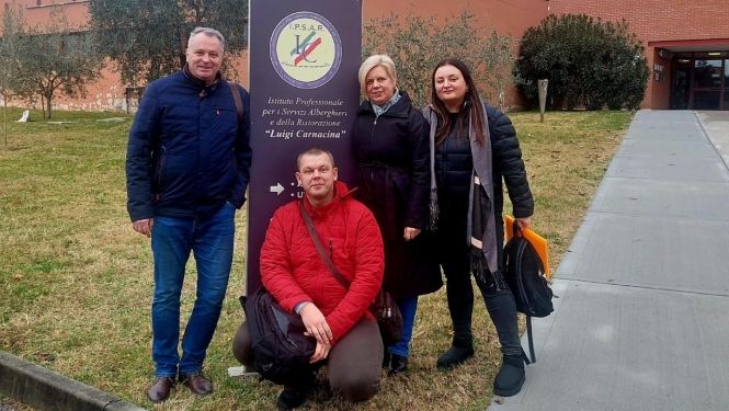 Četri tehnikuma pārstāvji pozē pie izglītības iestādes informatīvās zīmes ārpus ēkas