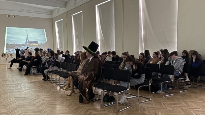Pasākuma dalībnieki sēž zālē un vēro projekta prezentāciju