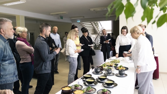Cilvēki degustē ēdienus pie servēta galda iekštelpās