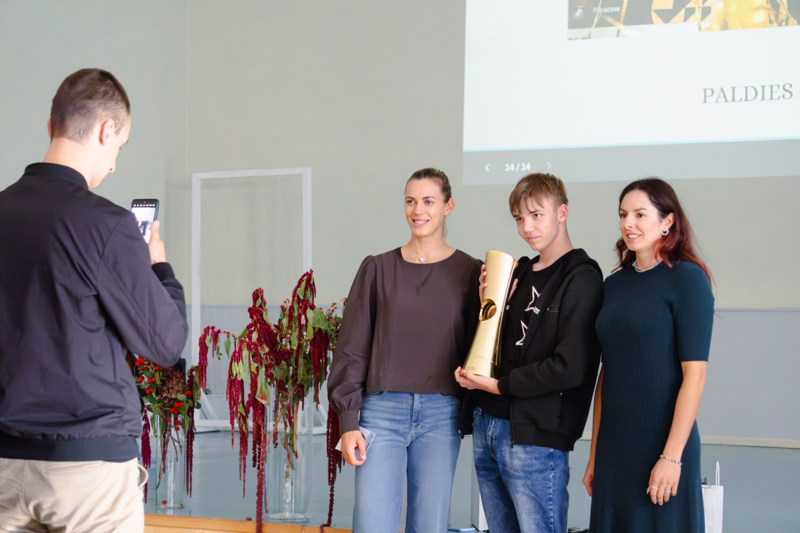 Izglītojamais tur rokās čempionu kausu, kopbilde ar sportistēm