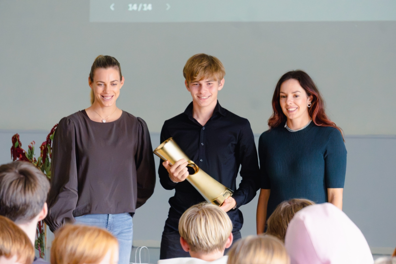Izglītojamais tur rokās čempionu kausu, kopbilde ar sportistēm