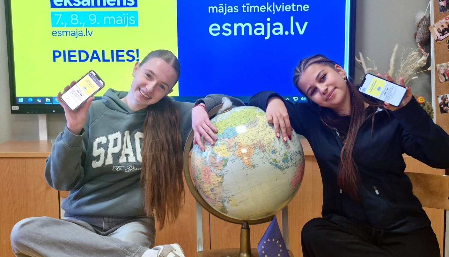 Divas meitenes klasē pie globusa tur telefonus ar informāciju par Eiropas eksāmenu