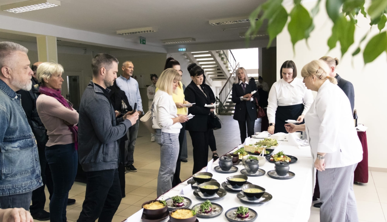 Cilvēki degustē ēdienus pie servēta galda iekštelpās