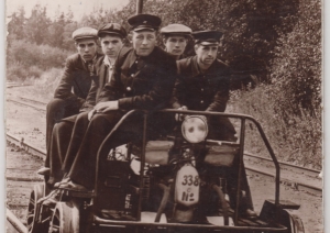 Vēsturiska fotogrāfija ar pieciem topošajiem dzelzceļa speciālistiem uz sliežu motorratiņiem