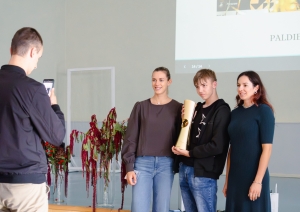 Izglītojamais tur rokās čempionu kausu, kopbilde ar sportistēm